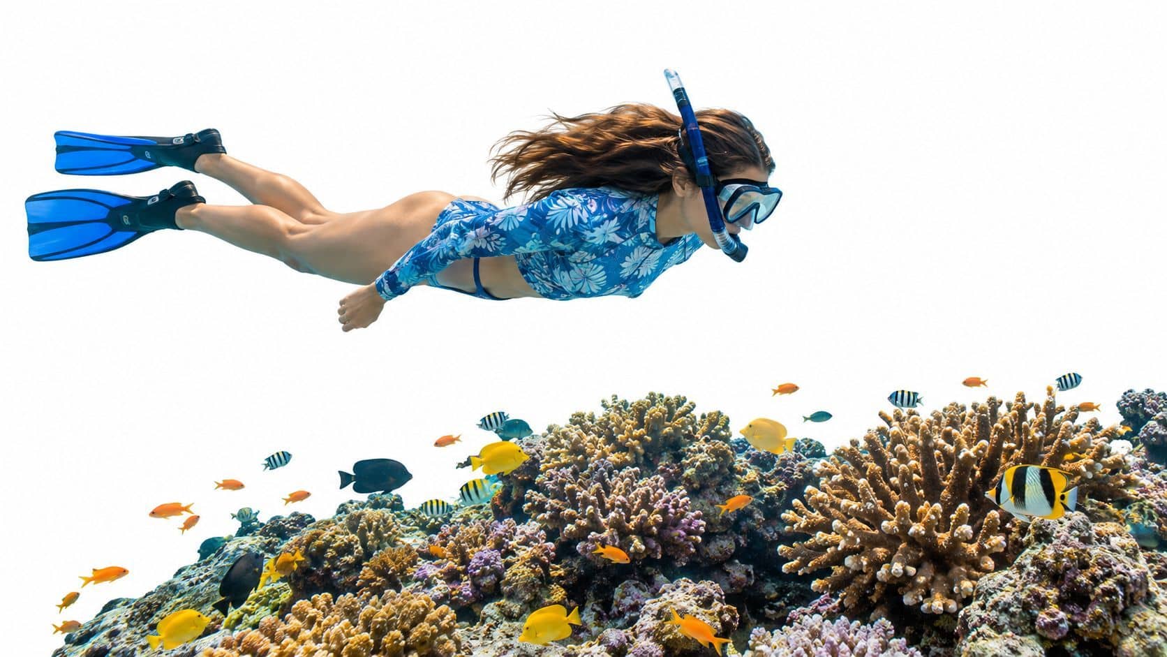 A woman snorkeling above a vibrant coral reef filled with colorful tropical fish in crystal clear water.