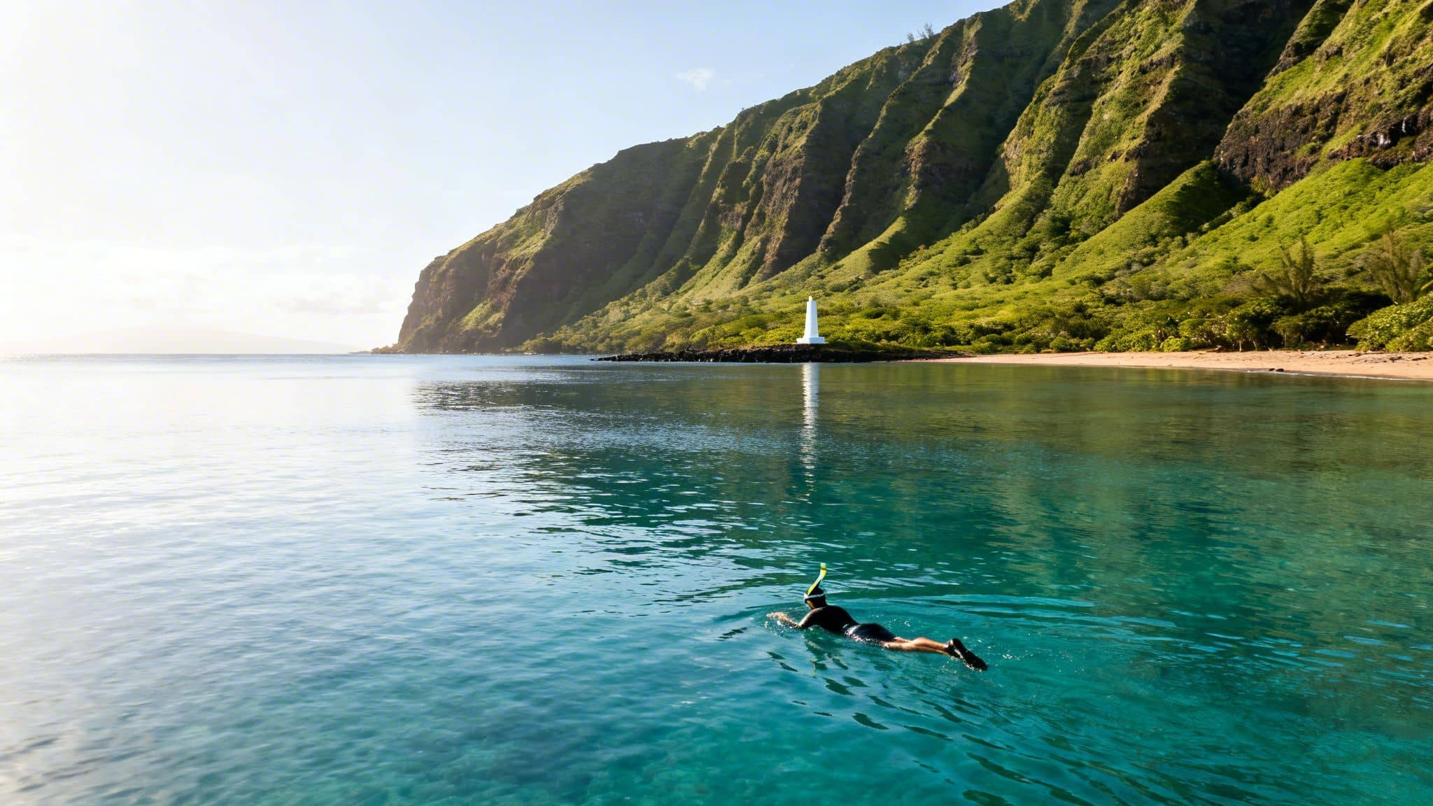 A person snorkeling in clear turquoise water near a beach, a white lighthouse, and lush green mountains.