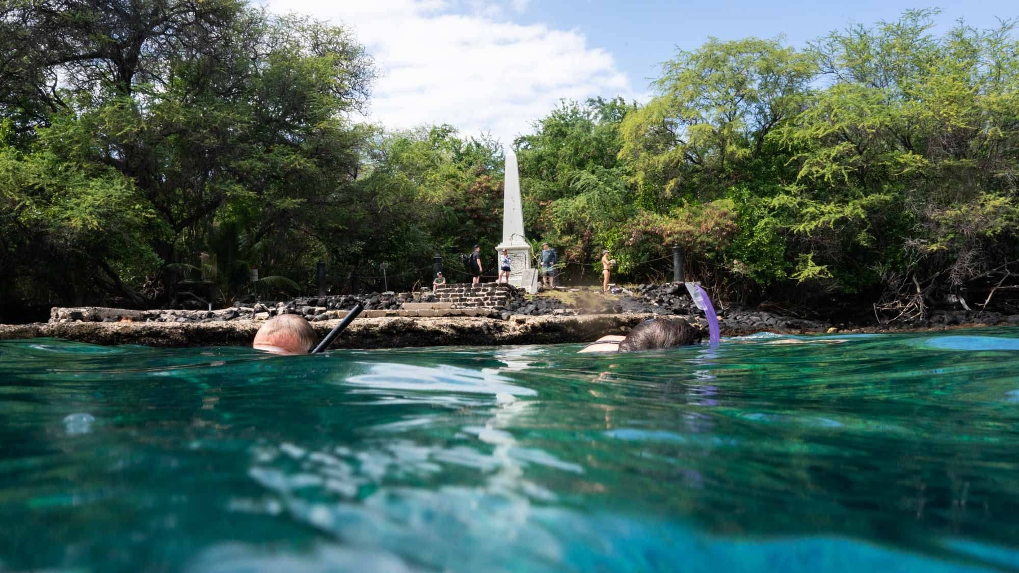 Snorkelers in clear water in front of the Captain Cook Monument