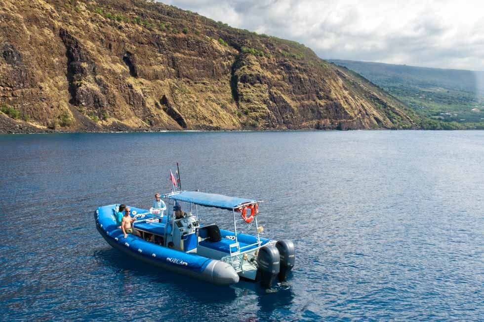 The blue Captain Cook RHIB idling beneath the Kealakekua Bay cliffs